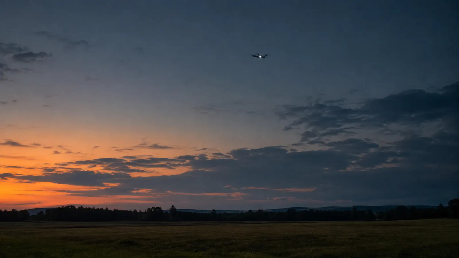 A drone with a strobe light visible as a bright dot in the sky at dusk over open fields