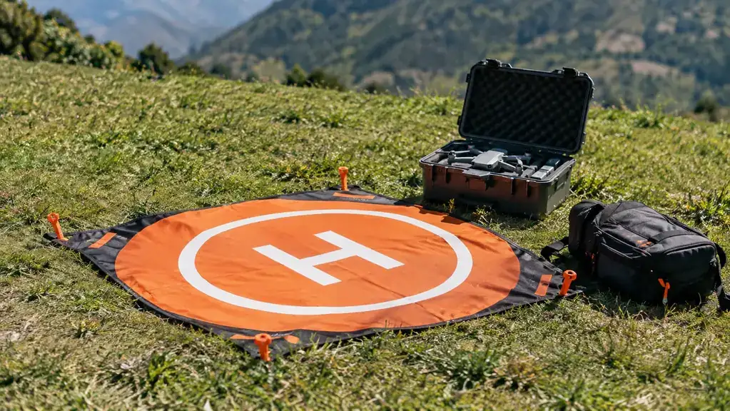 A landing pad laid flat on grass with stakes at the edges and a gear bag on one corner