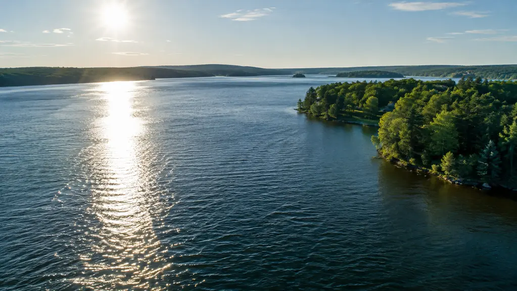 A drone flying low over a lake at midday, with glare on the water and a clear shoreline