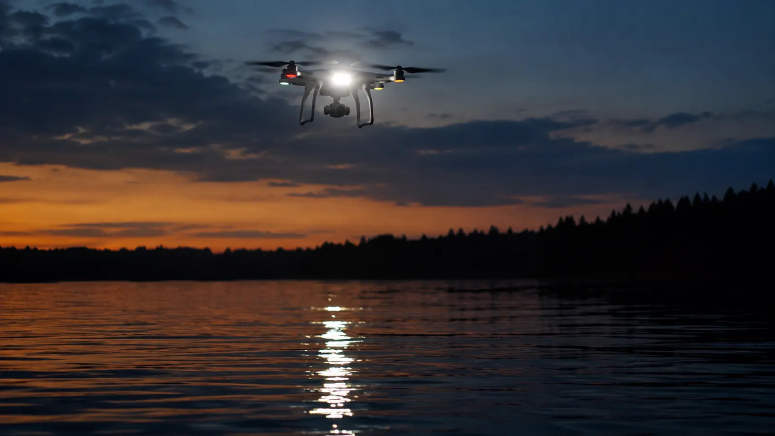A drone with a blinking light flying over a dark lake in the evening