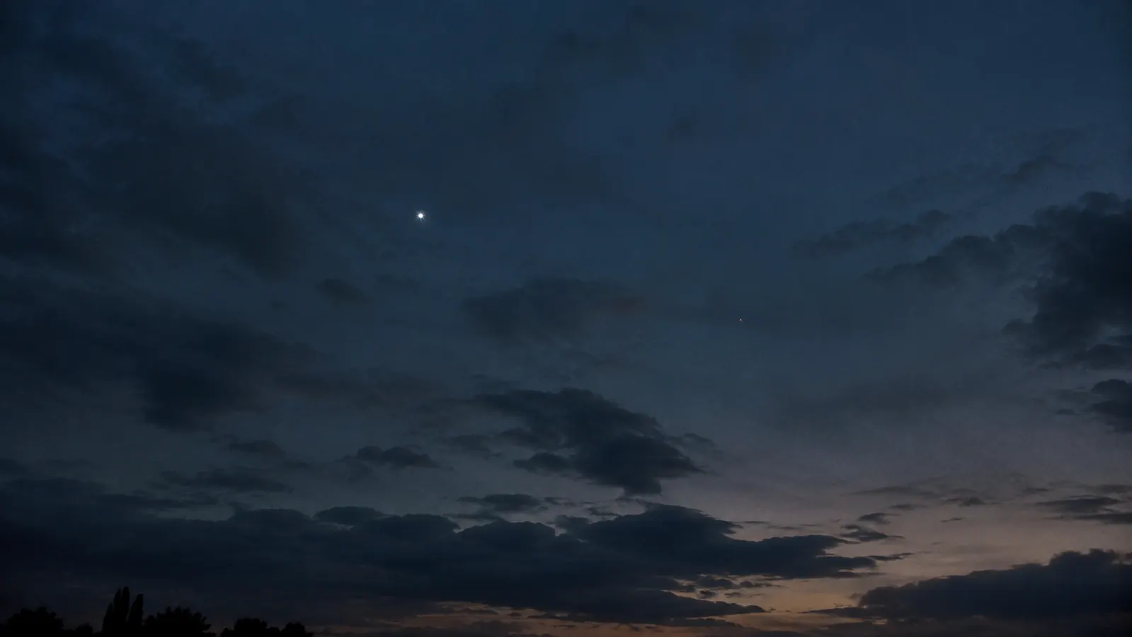 A wide view of a darkening sky with one small bright strobe light clearly visible and a faint small drone light nearly lost in the gloom